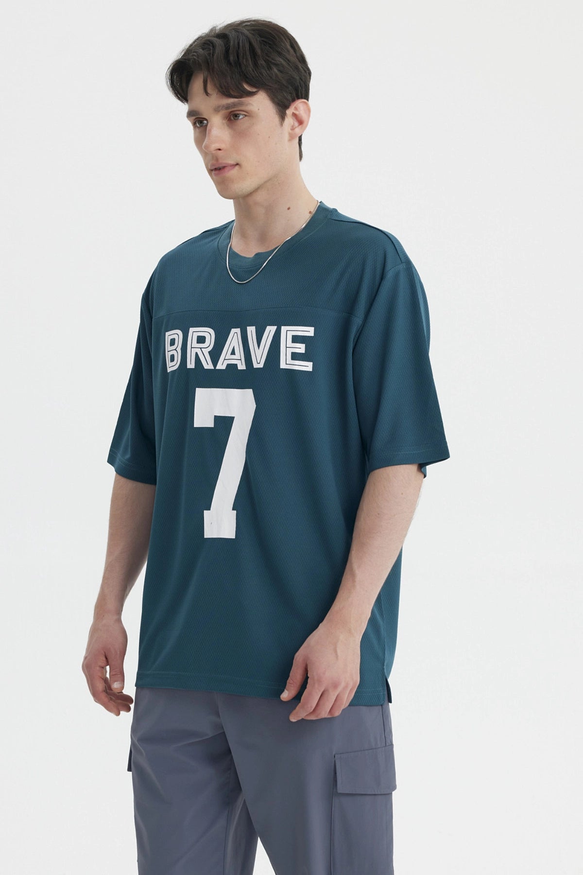 Polera oversize petróleo con texto BRAVE 7 en blanco centrado al frente estilo deportivo y casual