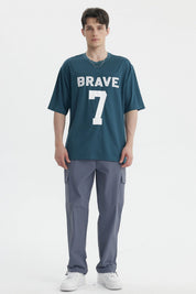 Polera oversize petróleo con texto BRAVE 7 en blanco centrado al frente estilo deportivo y casual