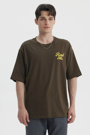 Polera oversize verde militar con estampado amarillo en el pecho que dice Road No Maps No Problems estilo casual relajado