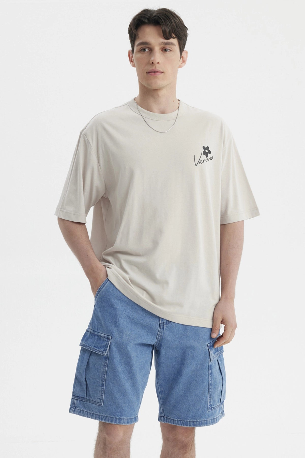 Polera beige de hombre con estampa pequeña en el pecho que dice Verano junto a una flor negra