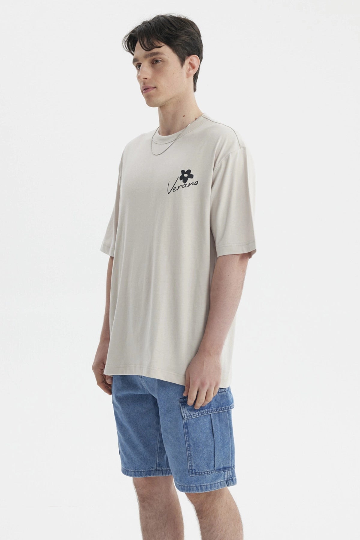 Polera beige de hombre con estampa pequeña en el pecho que dice Verano junto a una flor negra