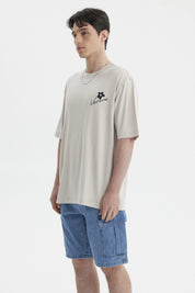Polera beige de hombre con estampa pequeña en el pecho que dice Verano junto a una flor negra