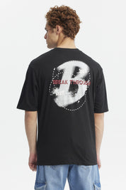 Polera oversize negra con estampado pequeño de letra H y texto Break Through en el pecho diseño moderno y minimalista