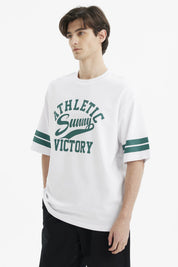 Polera oversize blanca para hombre con texto verde Athletic Sunny Victory al frente estilo casual y rayas en mangas