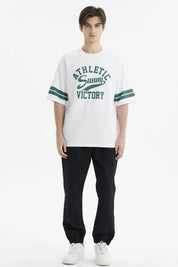 Polera oversize blanca para hombre con texto verde Athletic Sunny Victory al frente estilo casual y rayas en mangas