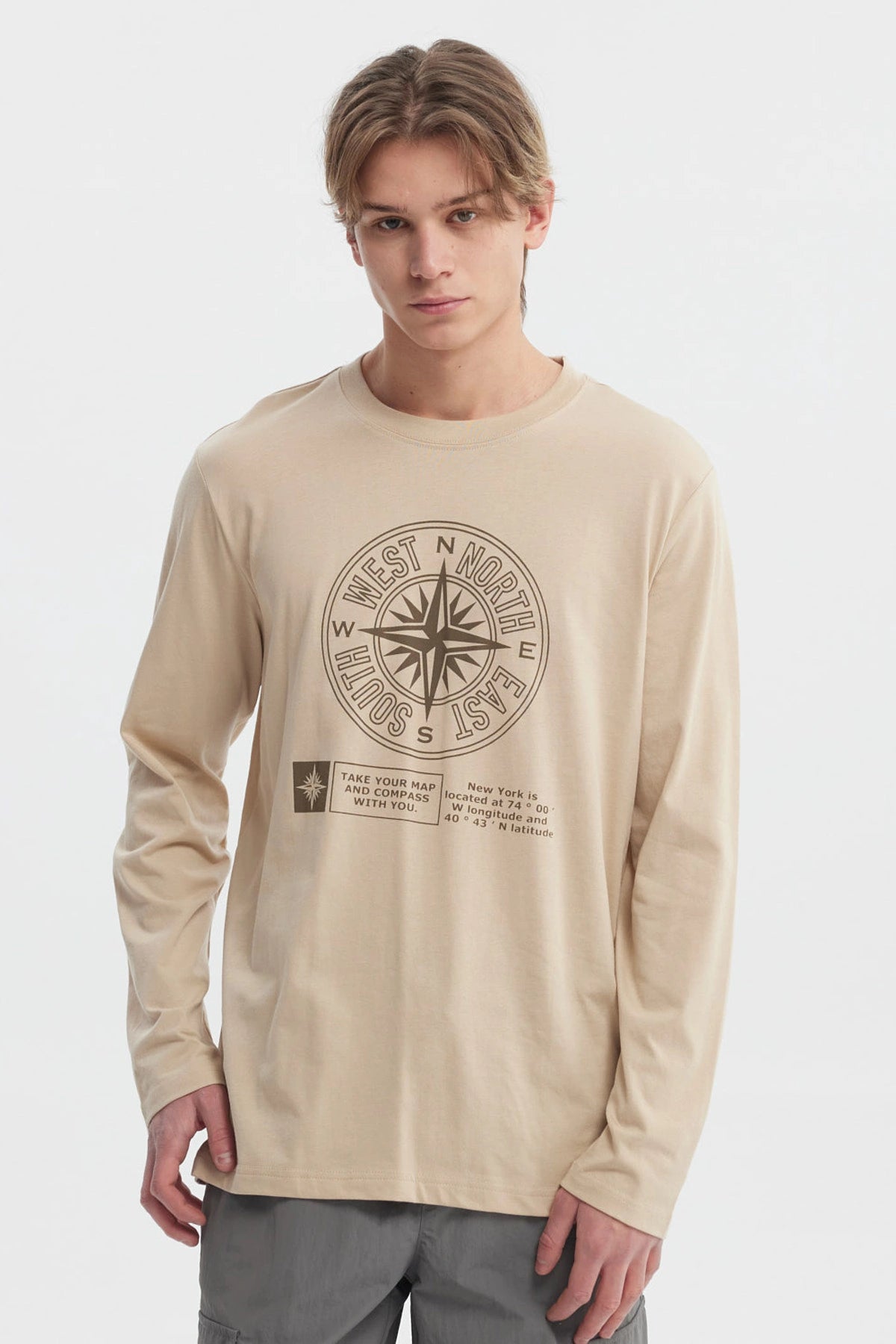 Polera beige oscuro hombre con brújula grande central y texto en el frente estilo casual relajado sin estampa trasera
