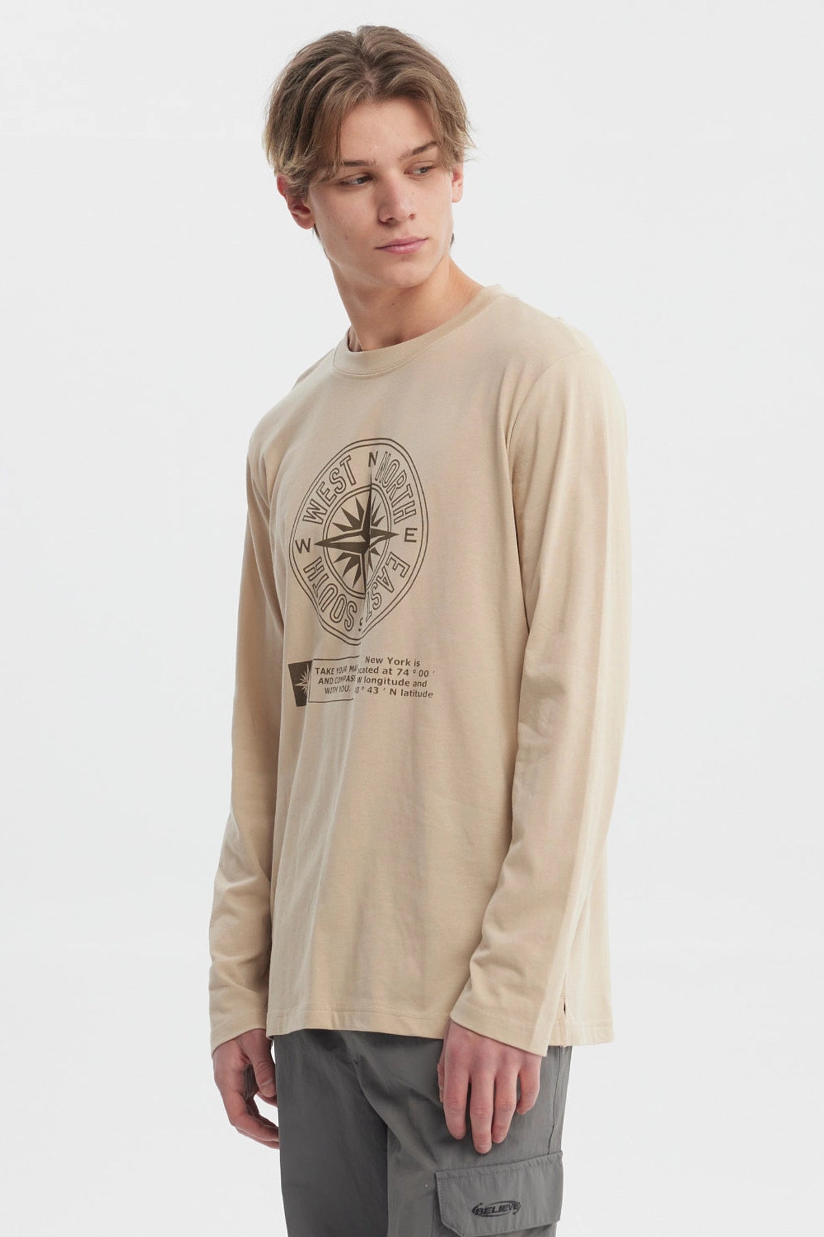 Polera beige oscuro hombre con brújula grande central y texto en el frente estilo casual relajado sin estampa trasera