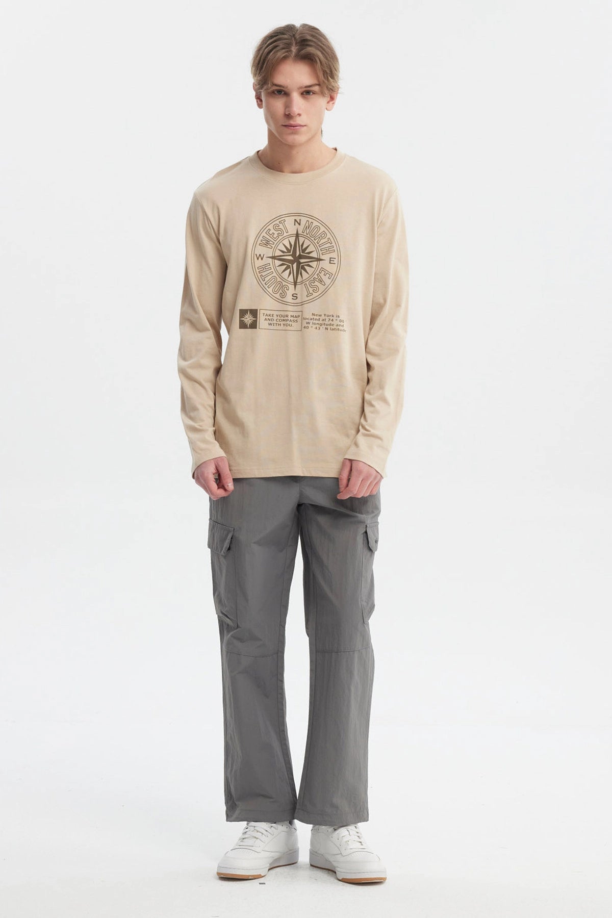 Polera beige oscuro hombre con brújula grande central y texto en el frente estilo casual relajado sin estampa trasera