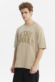 Polera oversize beige oscuro con texto Stay Awake en el pecho estilo casual relajado