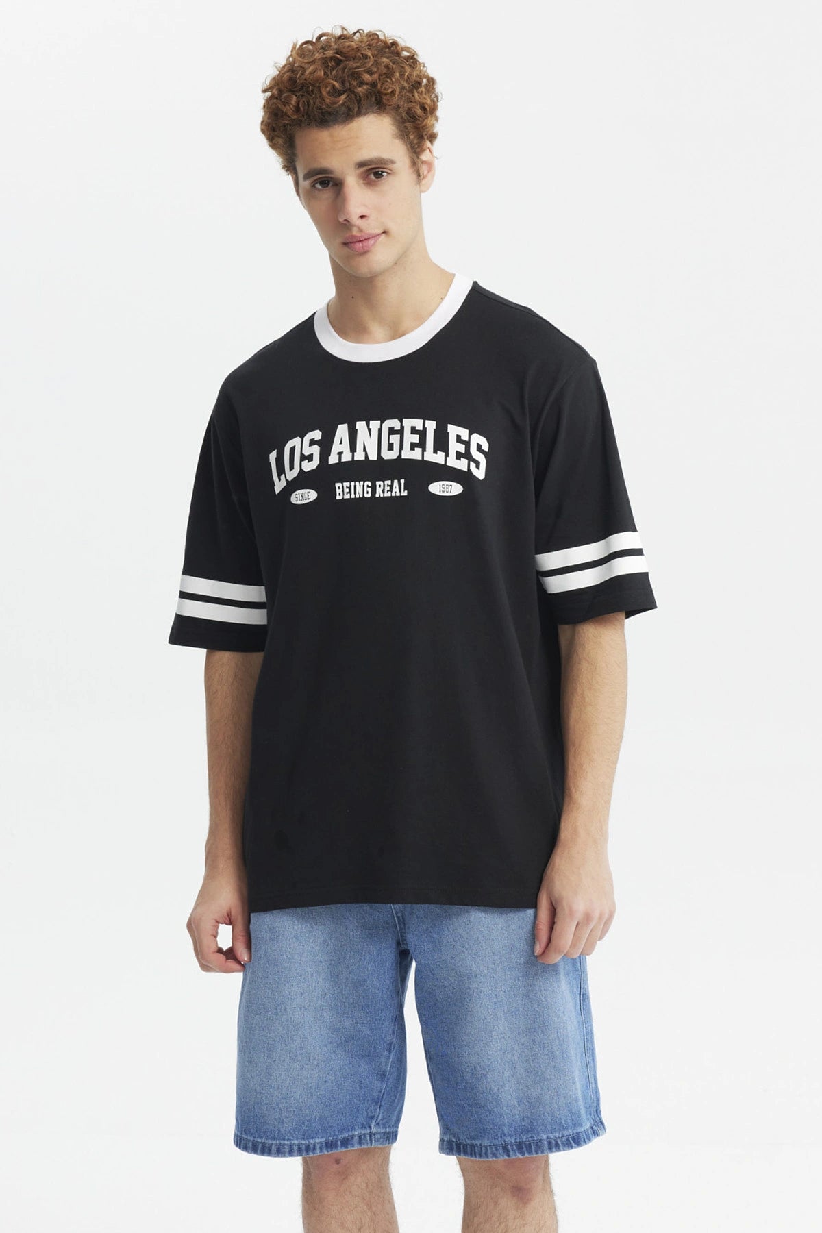 Polera negra hombre con texto Los Angeles Being Real al frente estilo urbano casual mangas con franjas blancas