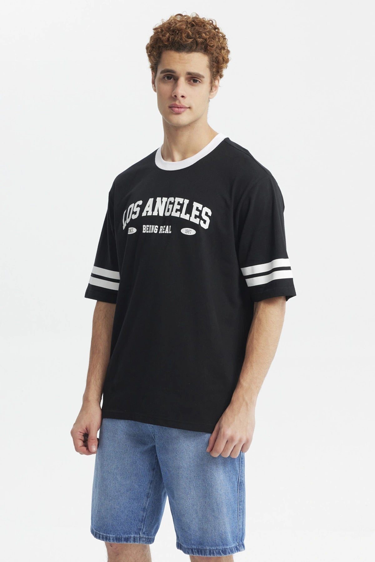 Polera negra hombre con texto Los Angeles Being Real al frente estilo urbano casual mangas con franjas blancas