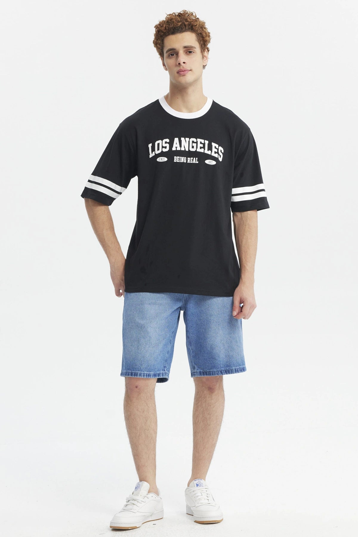 Polera negra hombre con texto Los Angeles Being Real al frente estilo urbano casual mangas con franjas blancas