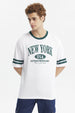 Polera blanca para hombre con texto New York USA Extraordinary en el pecho en verde y detalles de rayas en las mangas