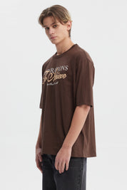 Polera slim chocolate para hombre con texto aspiracional al frente en estilo tipográfico clásico