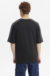 Polera negra oversize con doble línea blanca en mangas y estampado gráfico de texto pequeño en el pecho