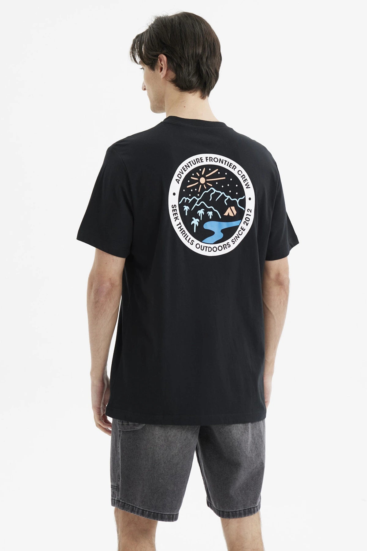Polera negra de hombre con estampado pequeño en el pecho de un paisaje montañoso con texto en círculo