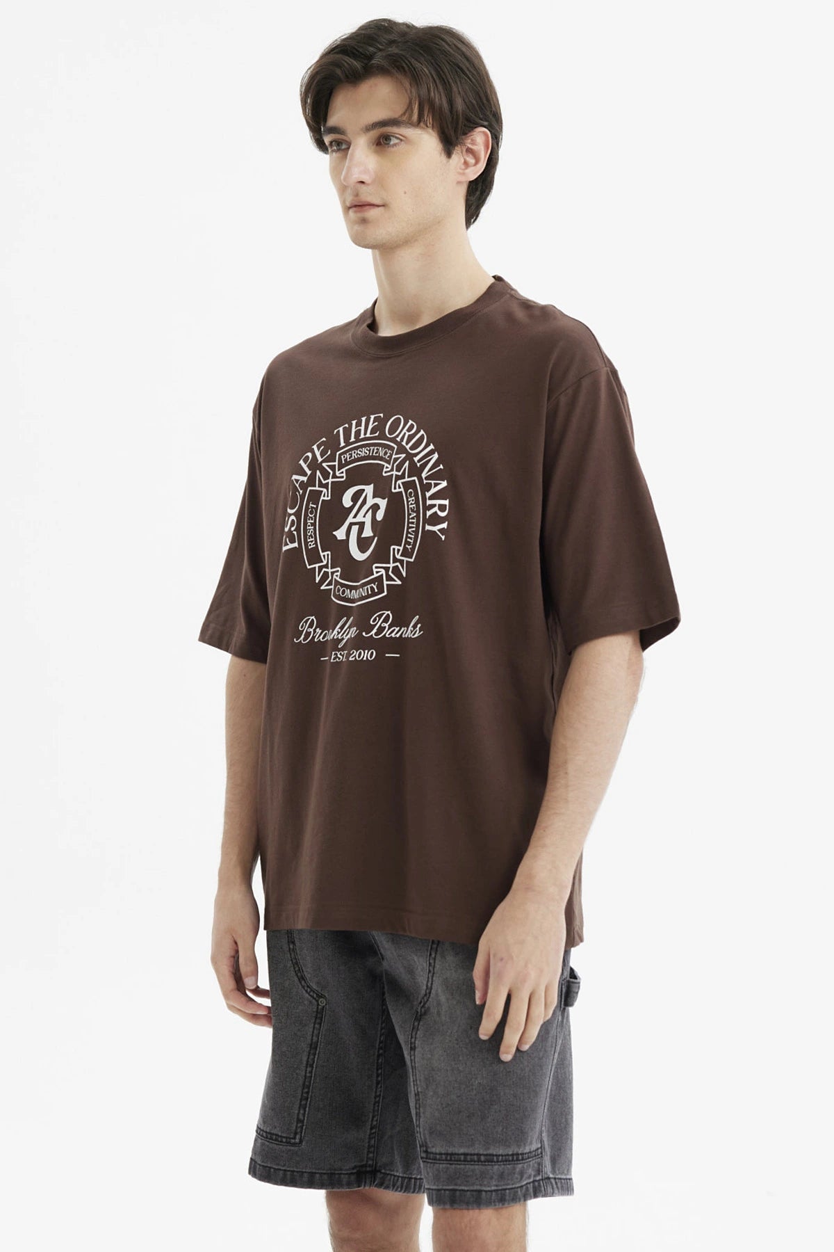 Polera oversize chocolate con estampado grande en el frente estilo universitario texto Escape the Ordinary