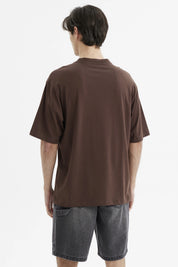 Polera oversize chocolate con estampado grande en el frente estilo universitario texto Escape the Ordinary