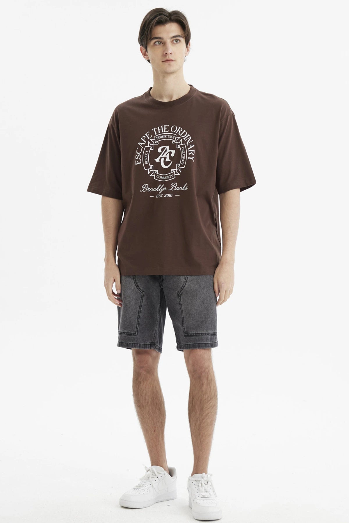 Polera oversize chocolate con estampado grande en el frente estilo universitario texto Escape the Ordinary