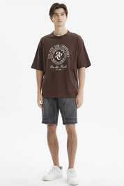 Polera oversize chocolate con estampado grande en el frente estilo universitario texto Escape the Ordinary