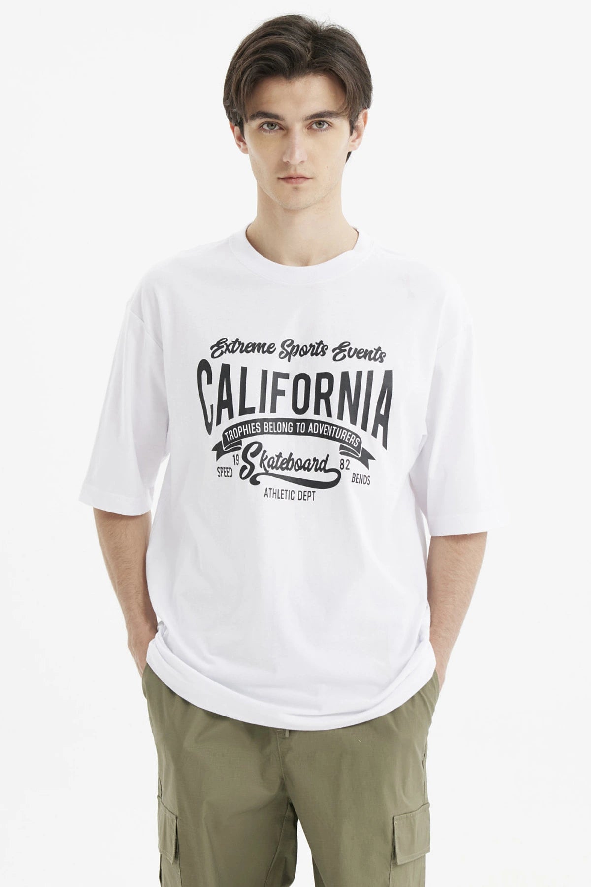 Polera oversize blanca para hombre con estampado grande central en negro que dice California y temática de eventos deportivos