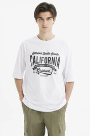 Polera oversize blanca para hombre con estampado grande central en negro que dice California y temática de eventos deportivos