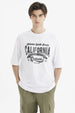 Polera oversize blanca para hombre con estampado grande central en negro que dice California y temática de eventos deportivos