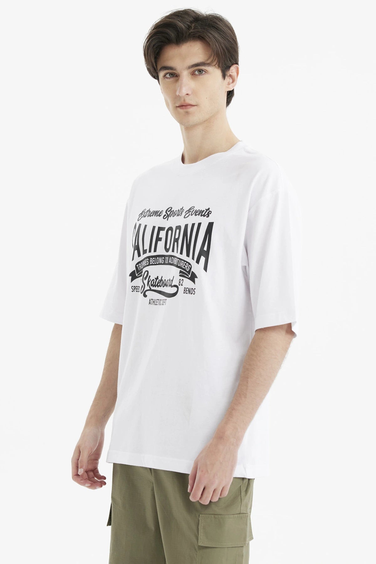 Polera oversize blanca para hombre con estampado grande central en negro que dice California y temática de eventos deportivos