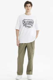 Polera oversize blanca para hombre con estampado grande central en negro que dice California y temática de eventos deportivos