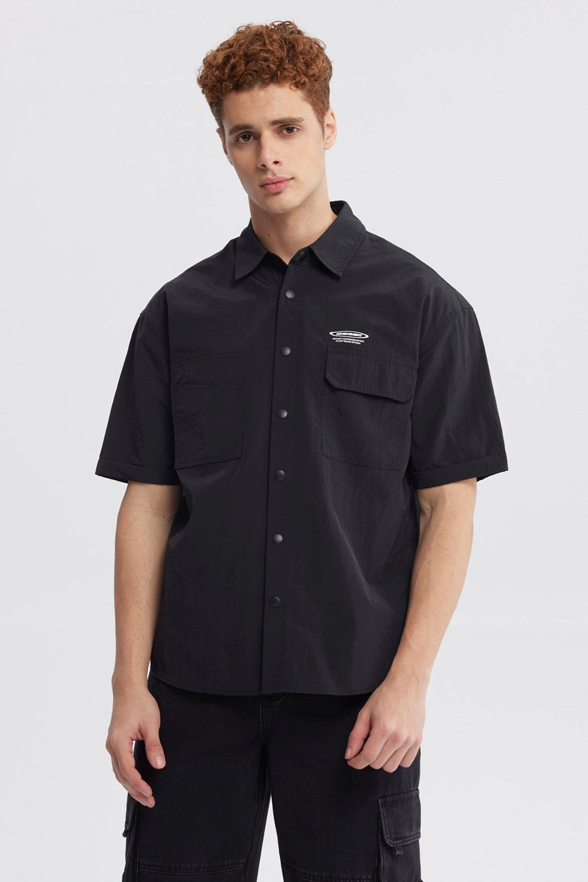 Camisa oversize negra de hombre con doble bolsillo y logo blanco en el pecho estilo casual sin estampa lisa