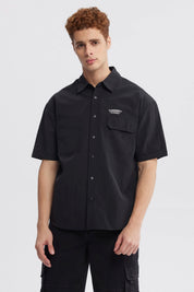 Camisa oversize negra de hombre con doble bolsillo y logo blanco en el pecho estilo casual sin estampa lisa
