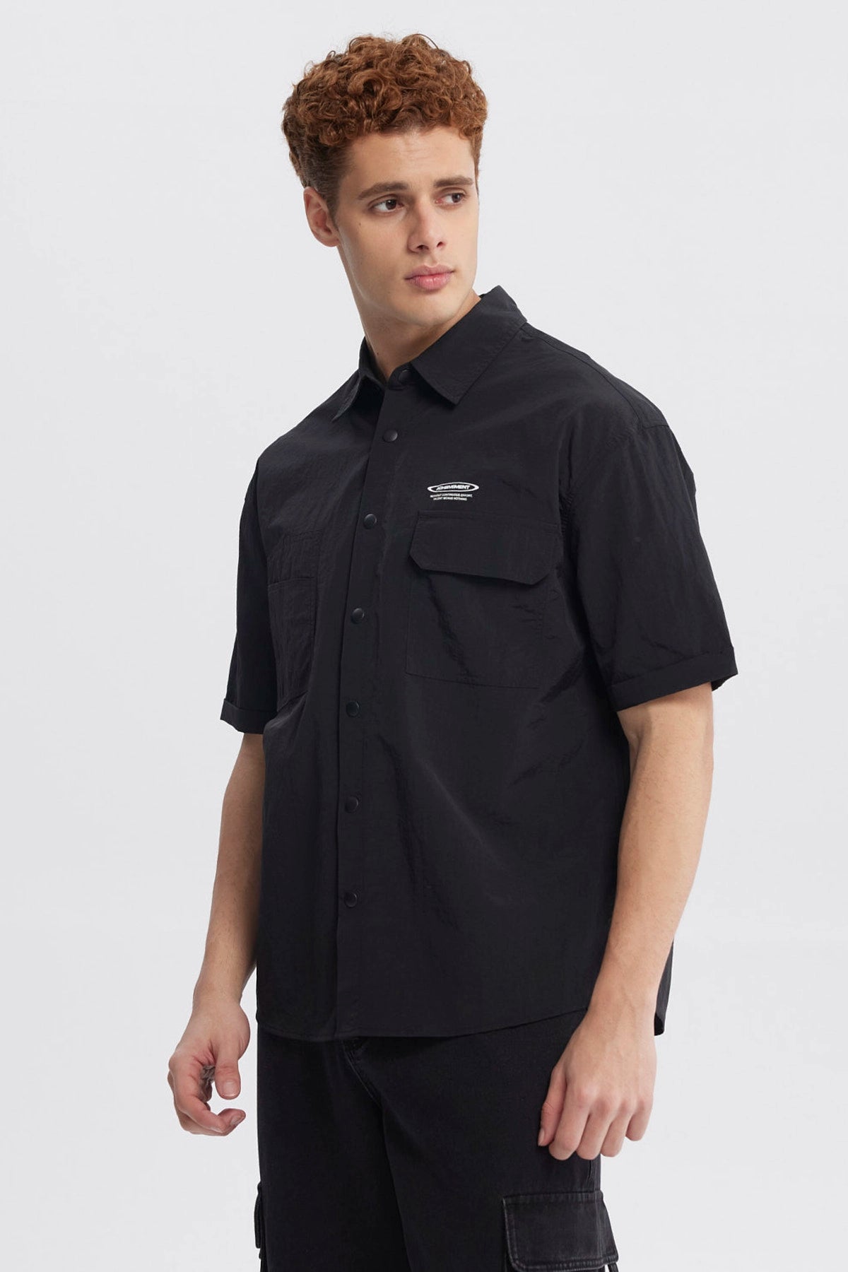 Camisa oversize negra de hombre con doble bolsillo y logo blanco en el pecho estilo casual sin estampa lisa