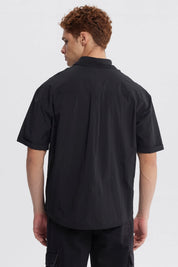 Camisa oversize negra de hombre con doble bolsillo y logo blanco en el pecho estilo casual sin estampa lisa