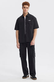Camisa oversize negra de hombre con doble bolsillo y logo blanco en el pecho estilo casual sin estampa lisa