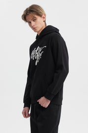 Polerón negro hombre con capucha y texto graffiti blanco al frente estilo urbano relajado
