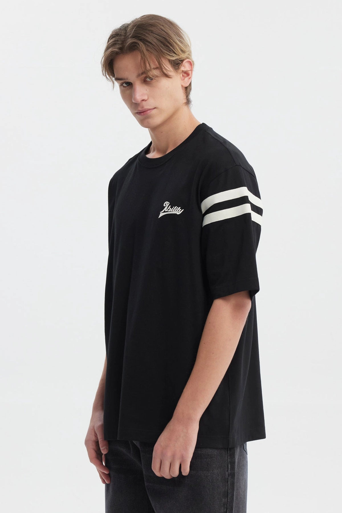 Polera oversize negra para hombre con texto Ability en el pecho y rayas blancas en mangas estilo casual