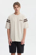 Polera oversize beige con logo "Critical" en el pecho estilo urbano y rayas marrones en las mangas
