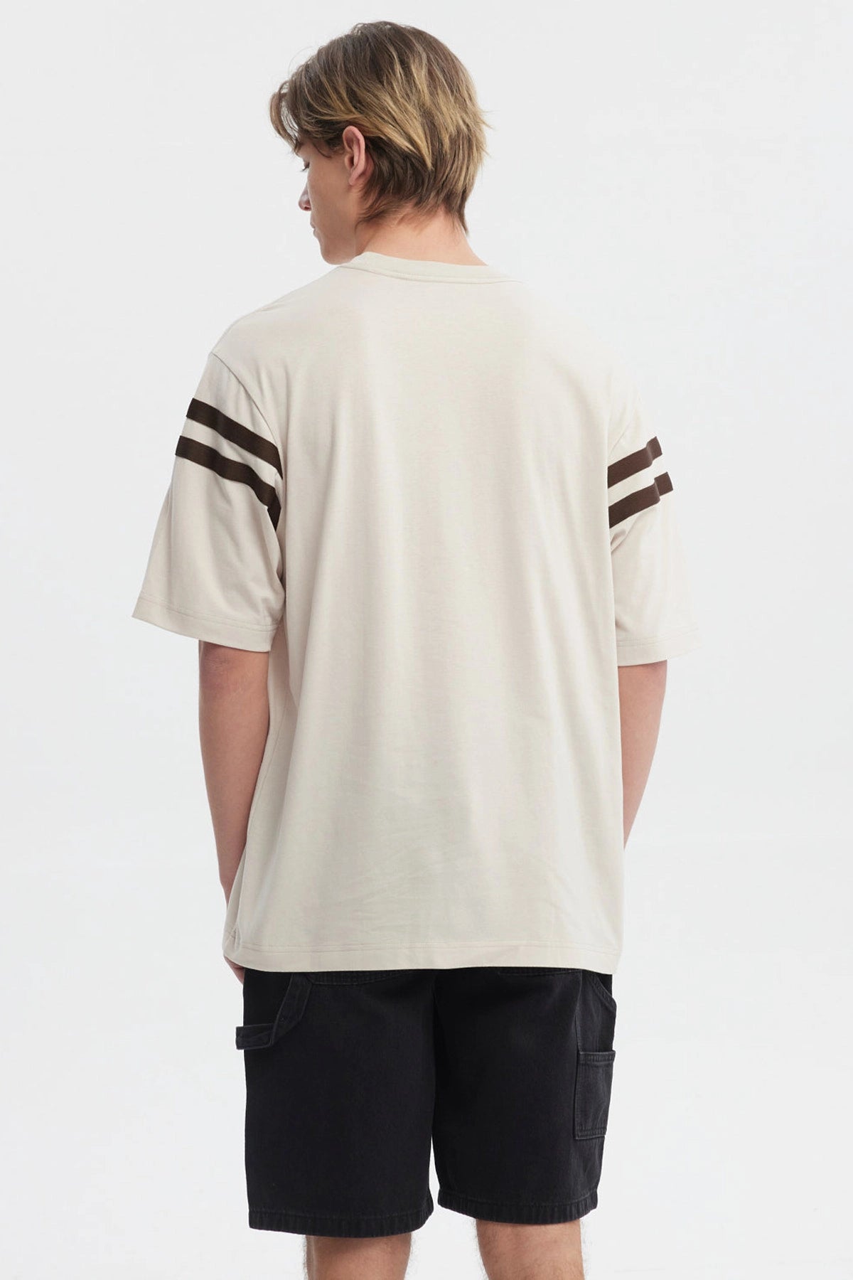Polera oversize beige con logo "Critical" en el pecho estilo urbano y rayas marrones en las mangas