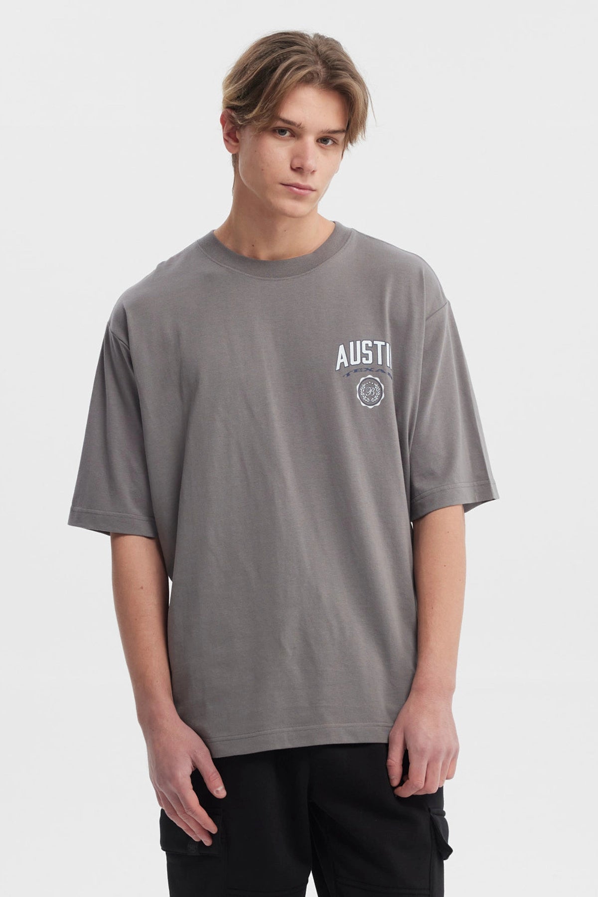 Polera hombre slim gris con estampa frontal de texto AUSTIN y escudo pequeño estilo casual
