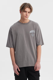 Polera hombre slim gris con estampa frontal de texto AUSTIN y escudo pequeño estilo casual