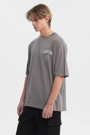 Polera hombre slim gris con estampa frontal de texto AUSTIN y escudo pequeño estilo casual